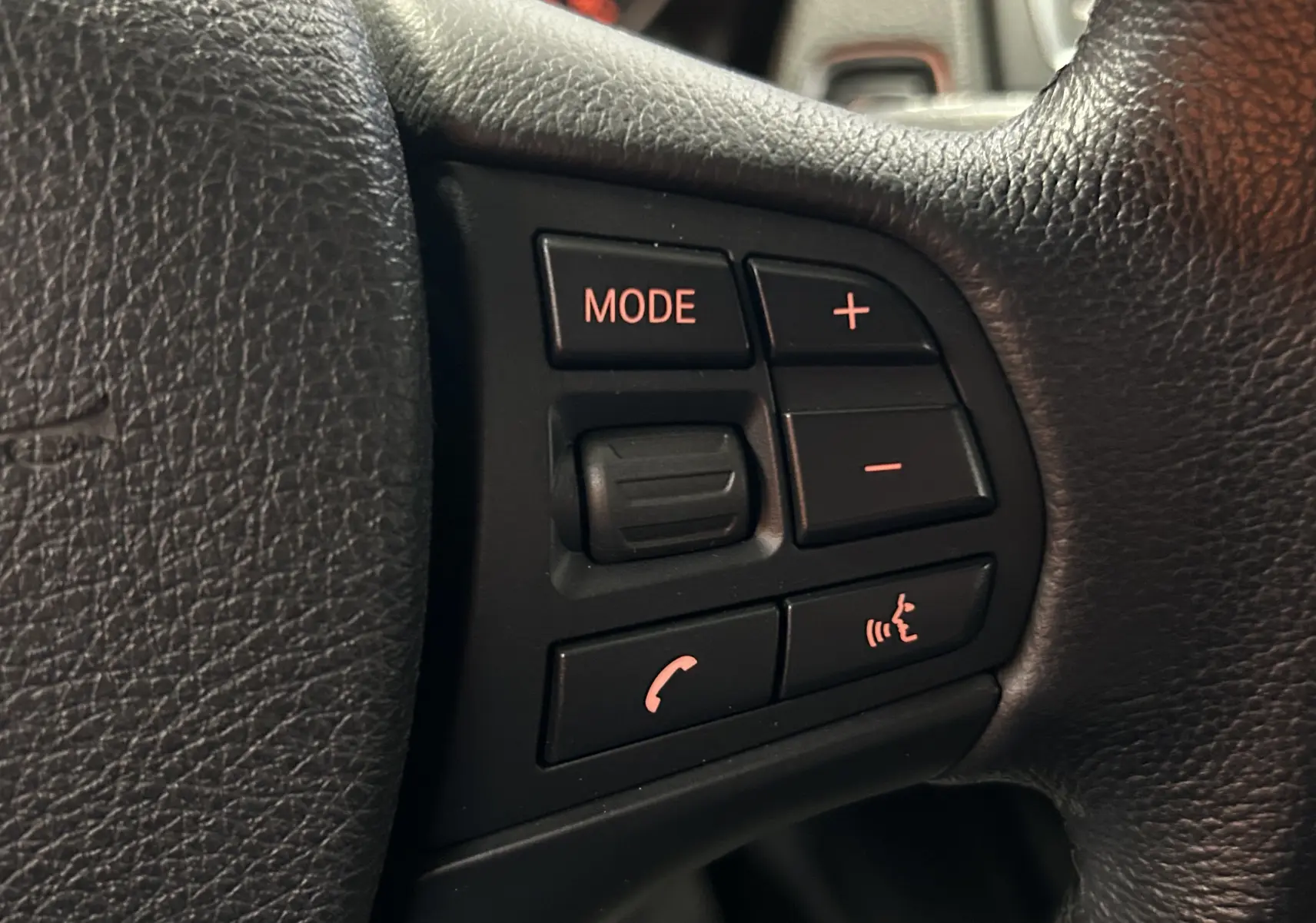 Gros plan sur les commandes au volant en cuir noir de la BMW Série 1 116d Business, boutons rétroéclairés rouges.