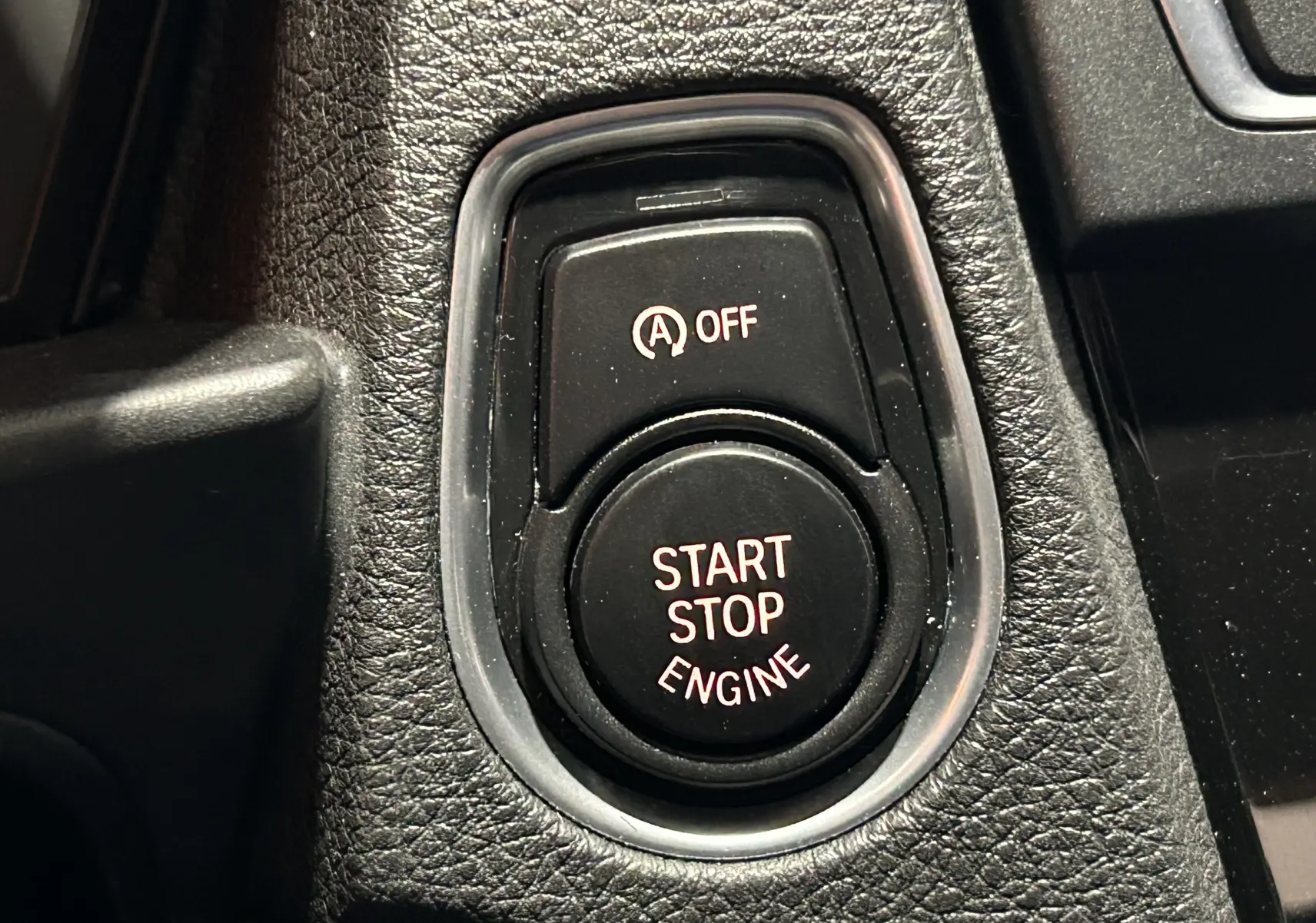 Gros plan sur le bouton Start Stop Engine noir entouré de plastique texturé dans une BMW Série 1 blanche de 2015.