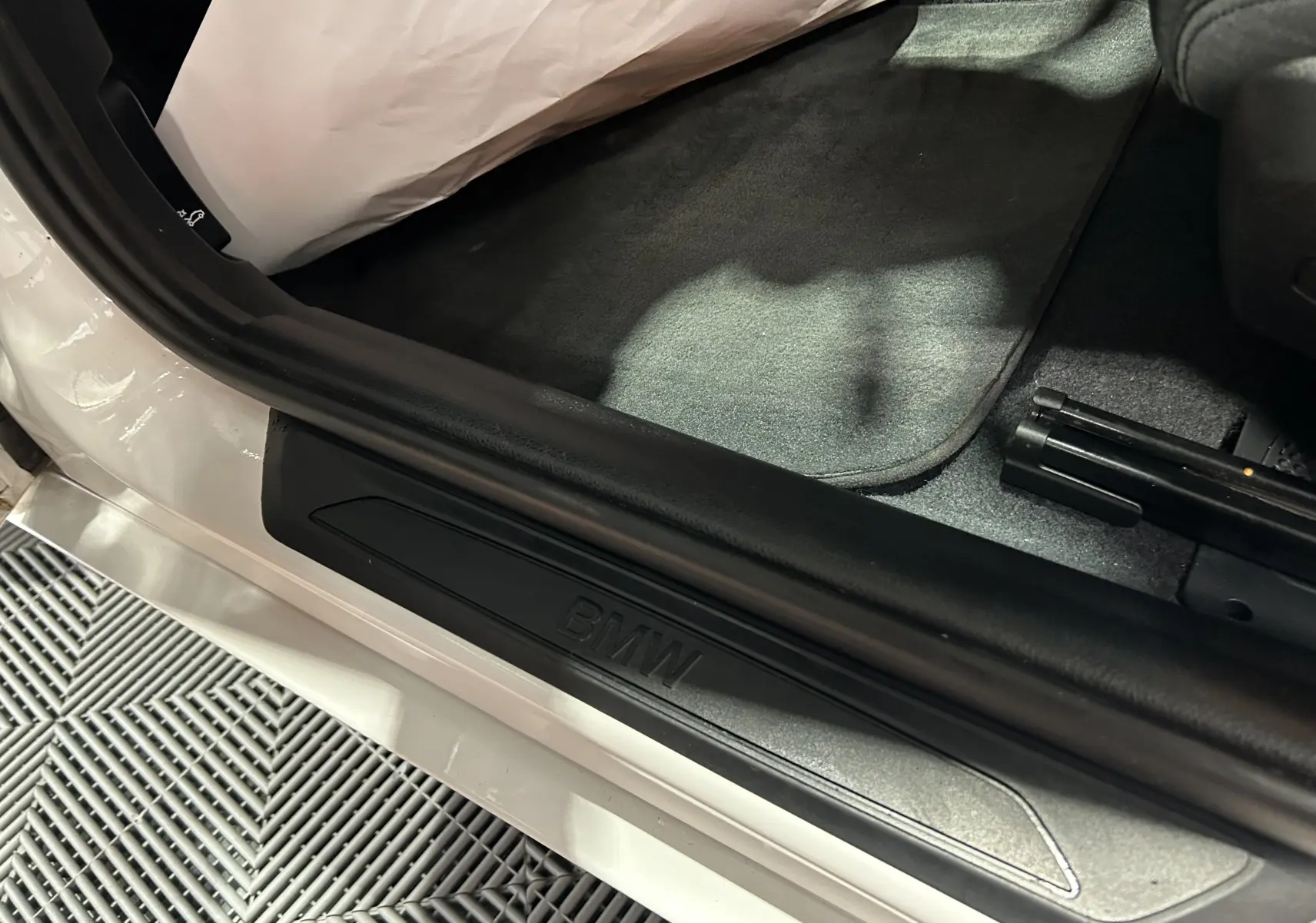 Gros plan sur le seuil de porte côté conducteur d'une BMW Série 1 blanche avec logo BMW en relief.
