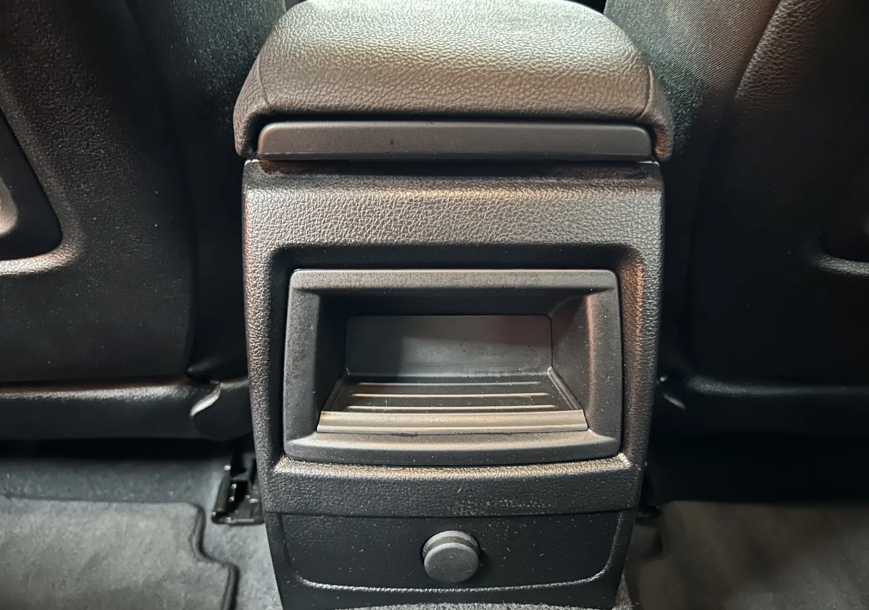 Détail de la console arrière noire de la BMW Série 1 116d Business 2015, avec rangement et prise 12V visible.