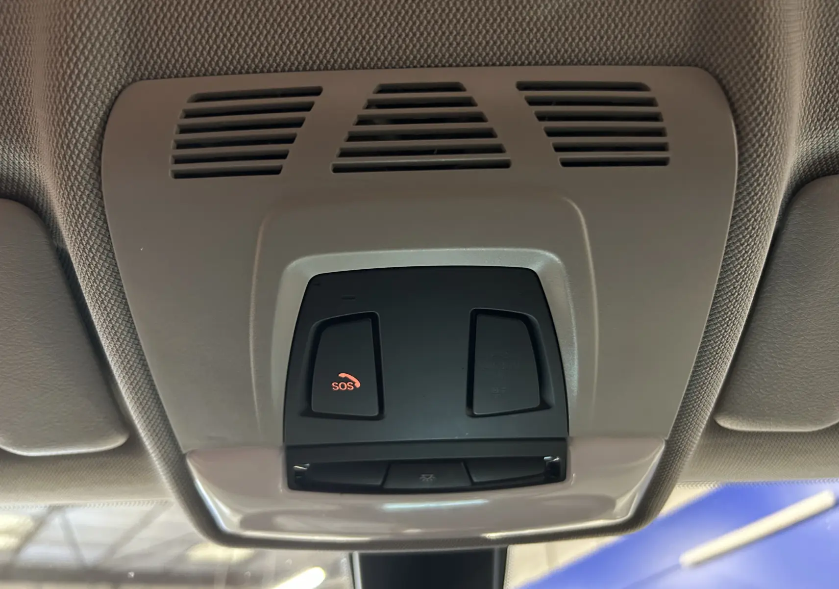 Vue en gros plan du plafonnier intérieur gris clair avec bouton SOS rouge de la BMW Série 1 116d Business 2015 blanche.