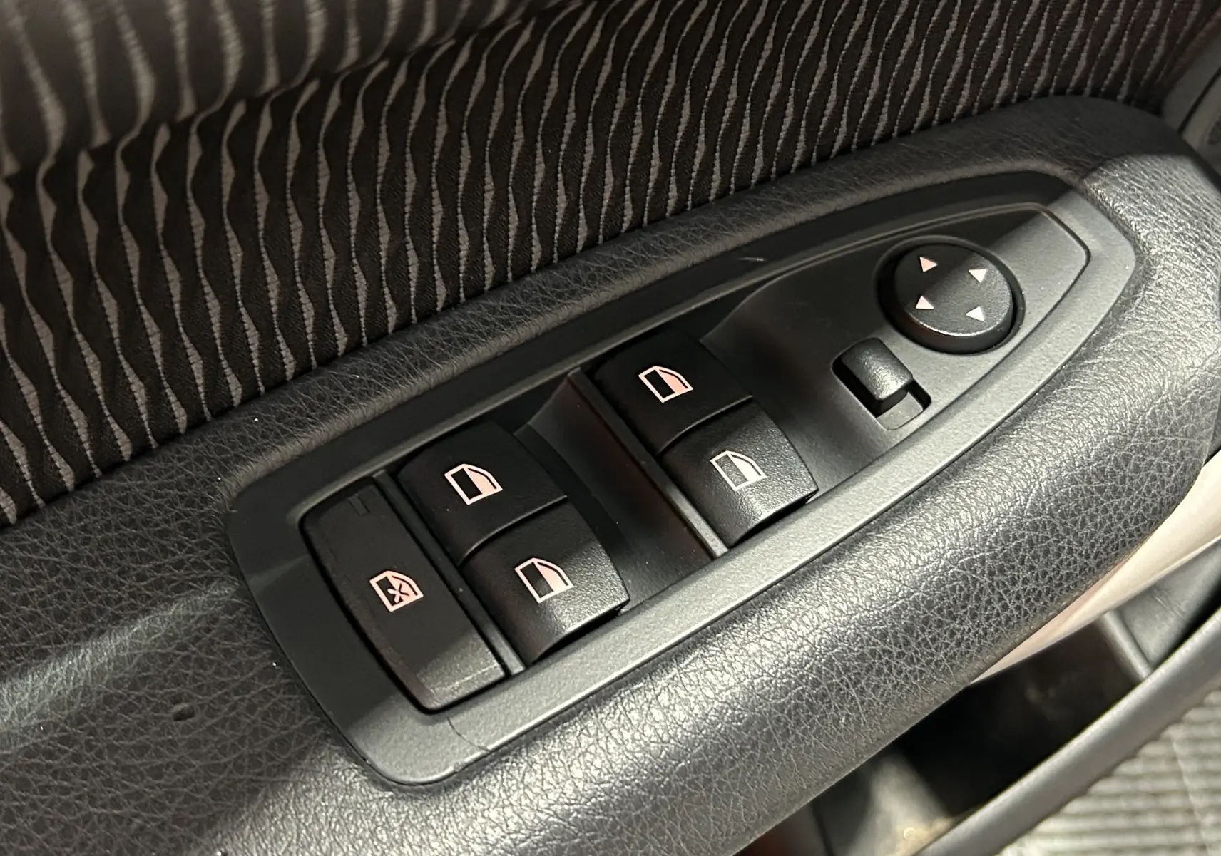 Gros plan sur les commandes de lève-vitres et réglage des rétroviseurs côté conducteur d'une BMW Série 1 blanche.