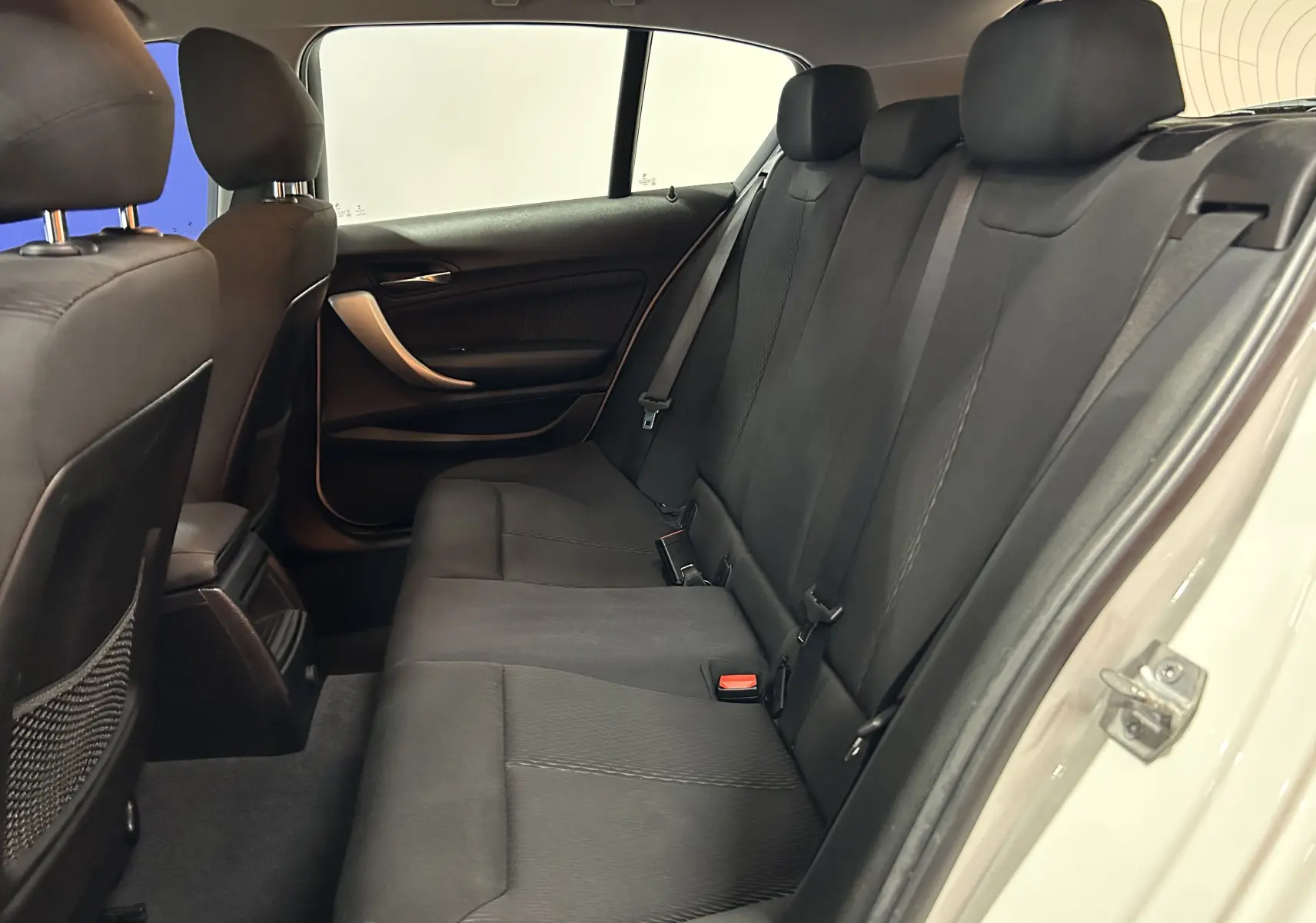 Vue intérieure côté droit des sièges arrière noirs d'une BMW Série 1 blanche, montrant les ceintures et les appuie-têtes.