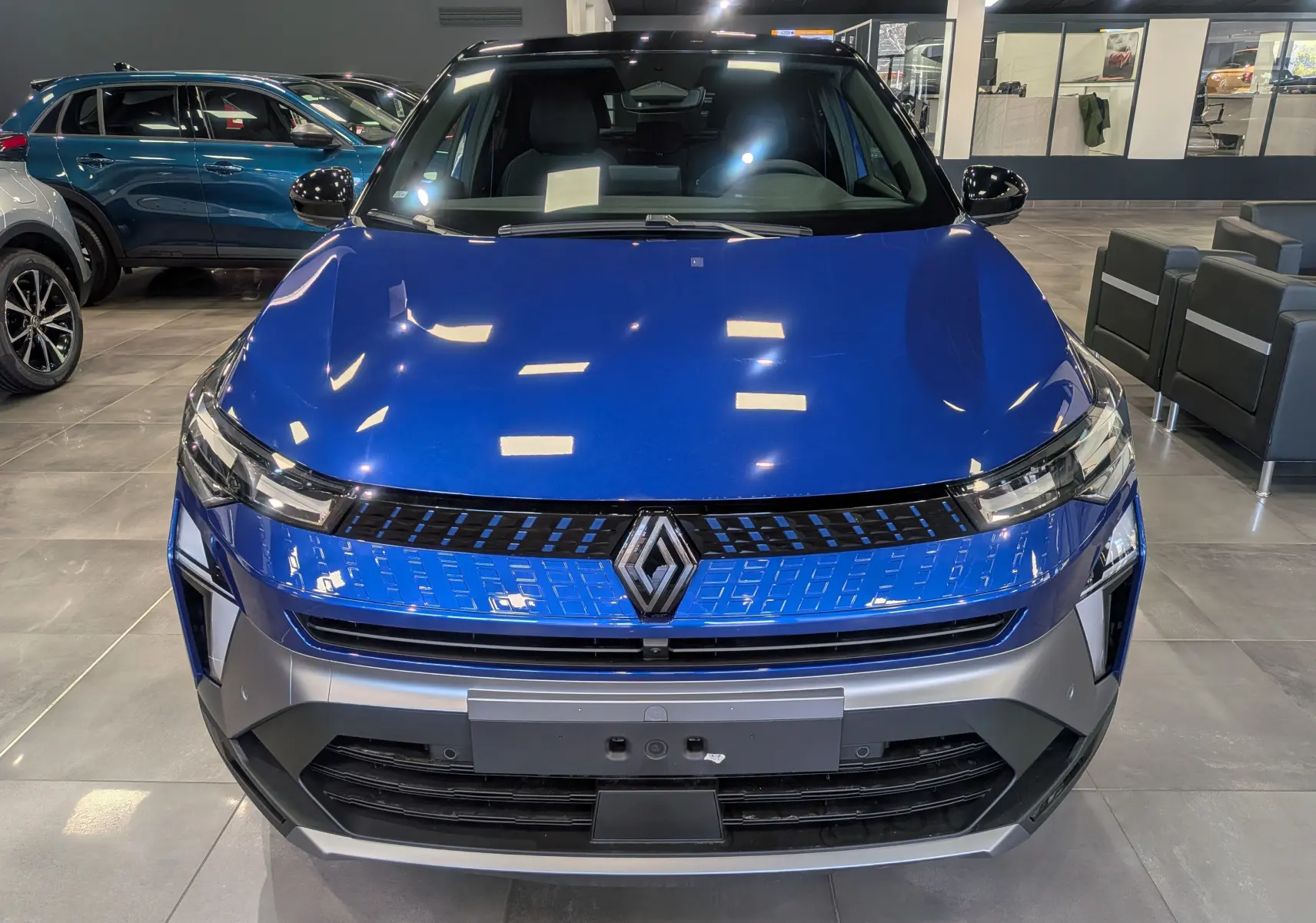 Vue frontale d'un Renault Captur E-TECH hybride bleu Iron avec toit noir, éclairage LED et calandre moderne en showroom.