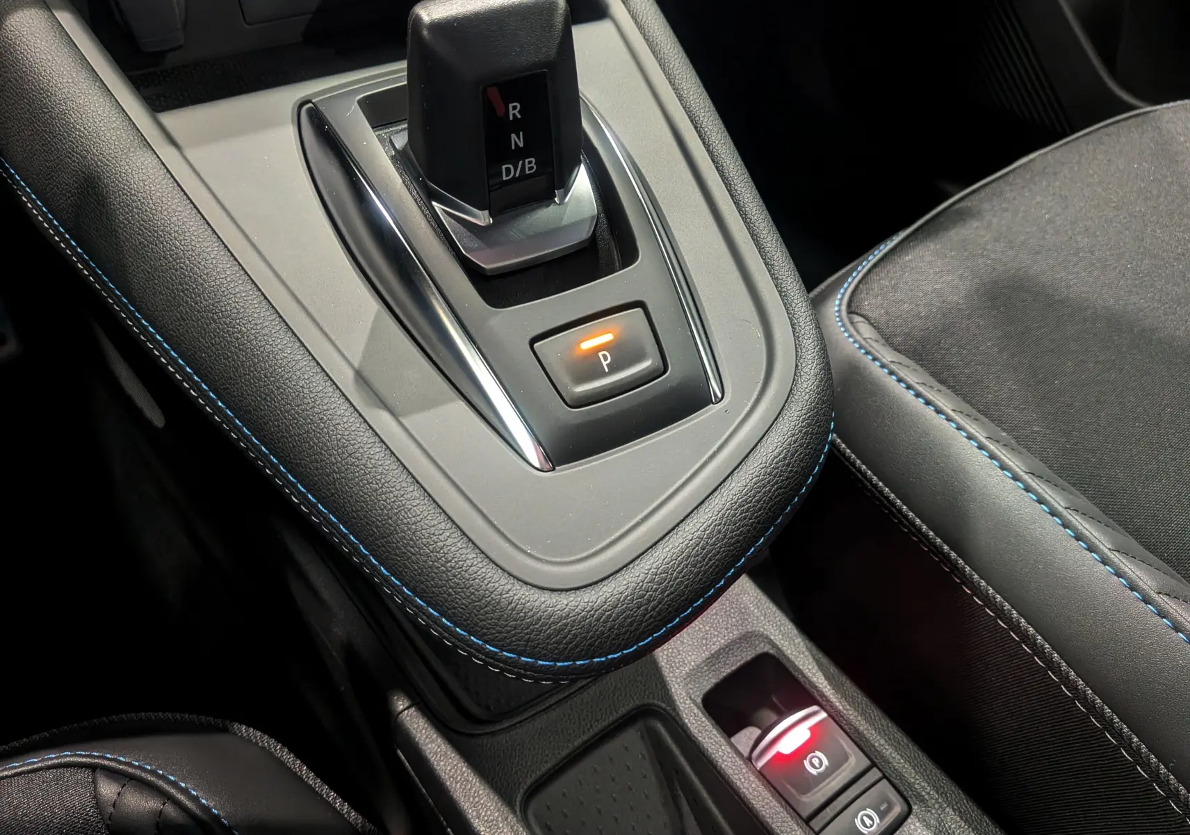 Gros plan sur la console centrale du Renault Captur E-TECH 2025, avec levier de vitesses et coutures bleues sur cuir noir.