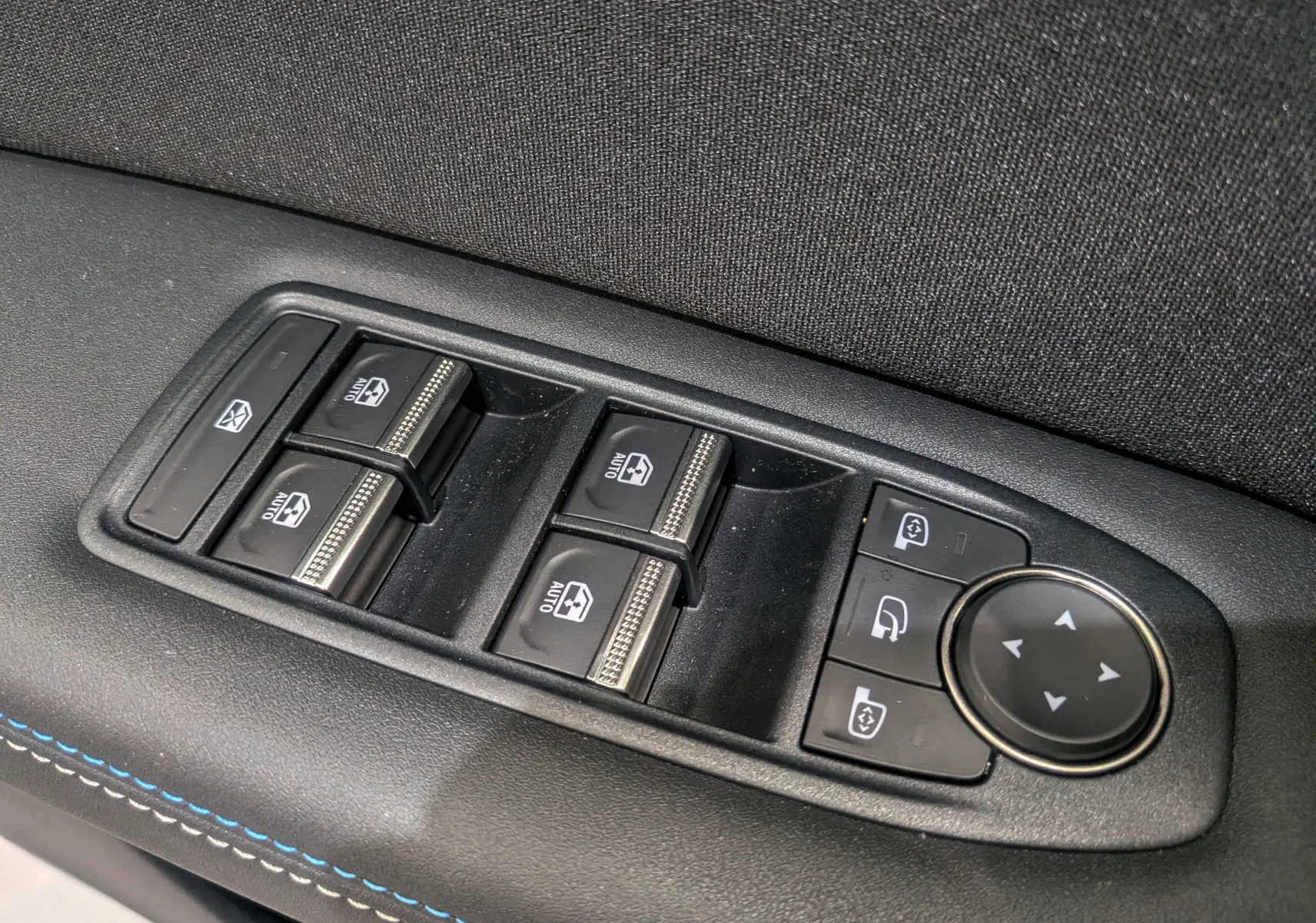 Panneau de commandes des vitres et rétroviseurs côté gauche avec surpiqûres bleues dans un Renault Captur E-Tech hybride 2025.