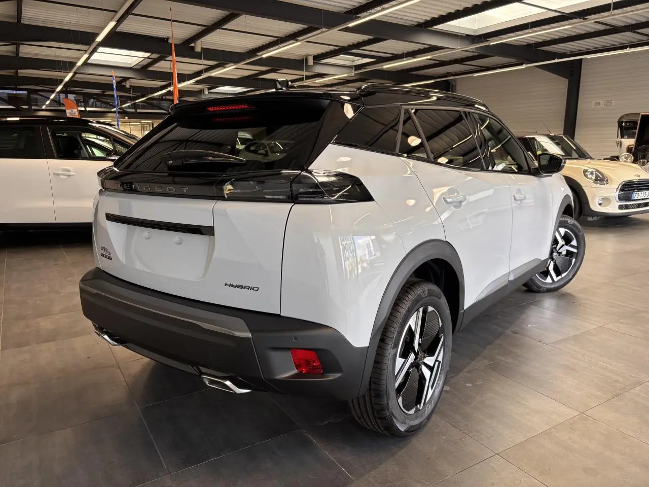 Vue 3/4 arrière droite d'un Peugeot 2008 blanc hybride 2025 avec toit noir et jantes distinctives en concession.