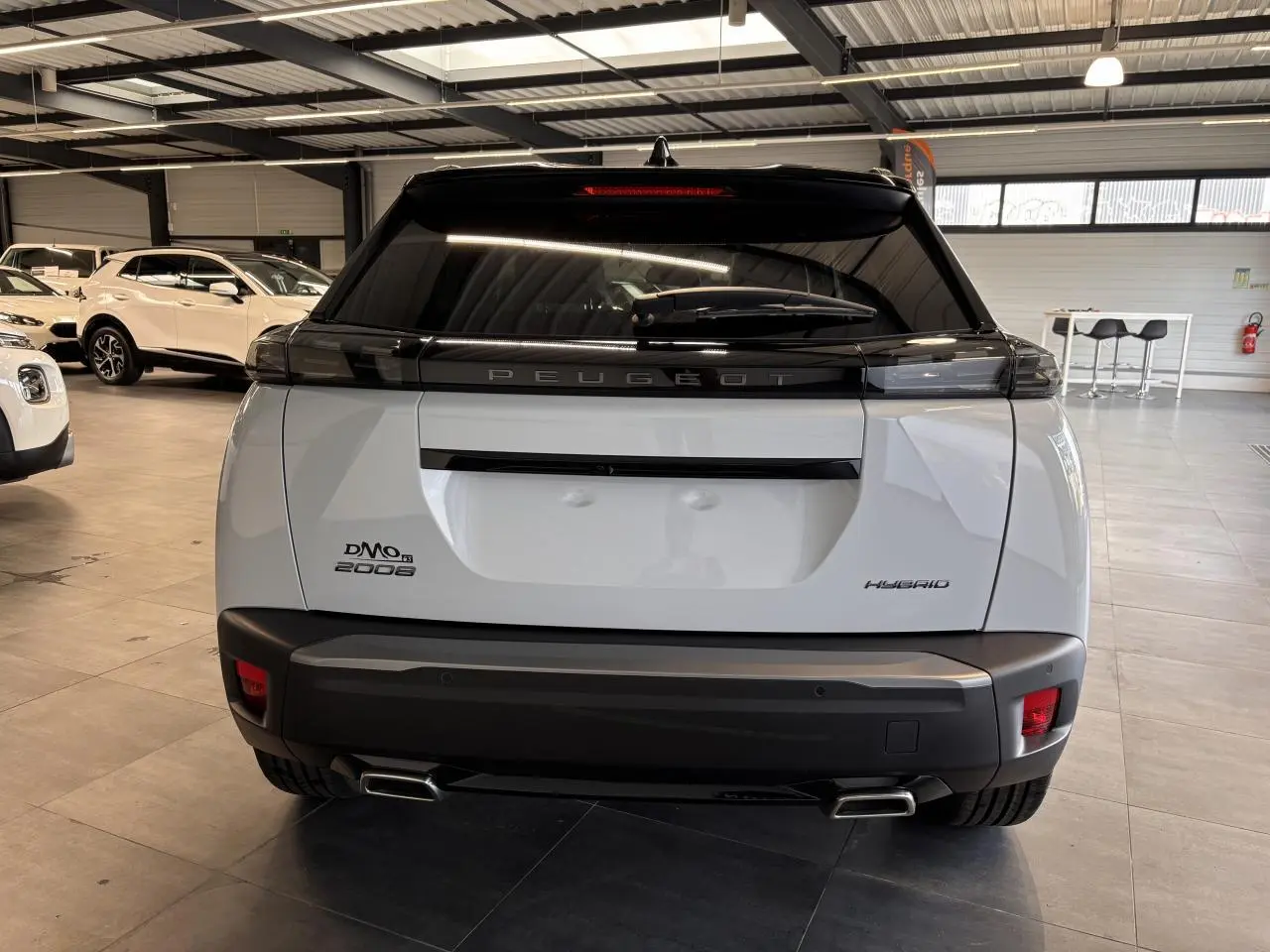 Vue arrière d'un Peugeot 2008 blanc hybride 2025 en intérieur, avec double sortie d'échappement et vitrage teinté noir.