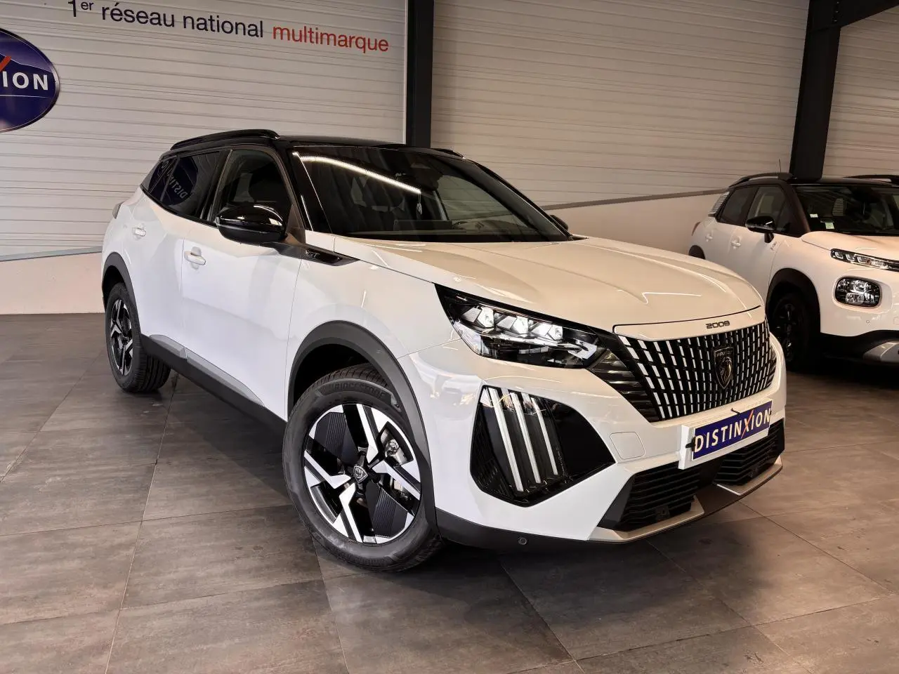 Peugeot 2008 blanc en 3/4 avant droit avec toit noir et calandre distinctive GT dans un showroom.