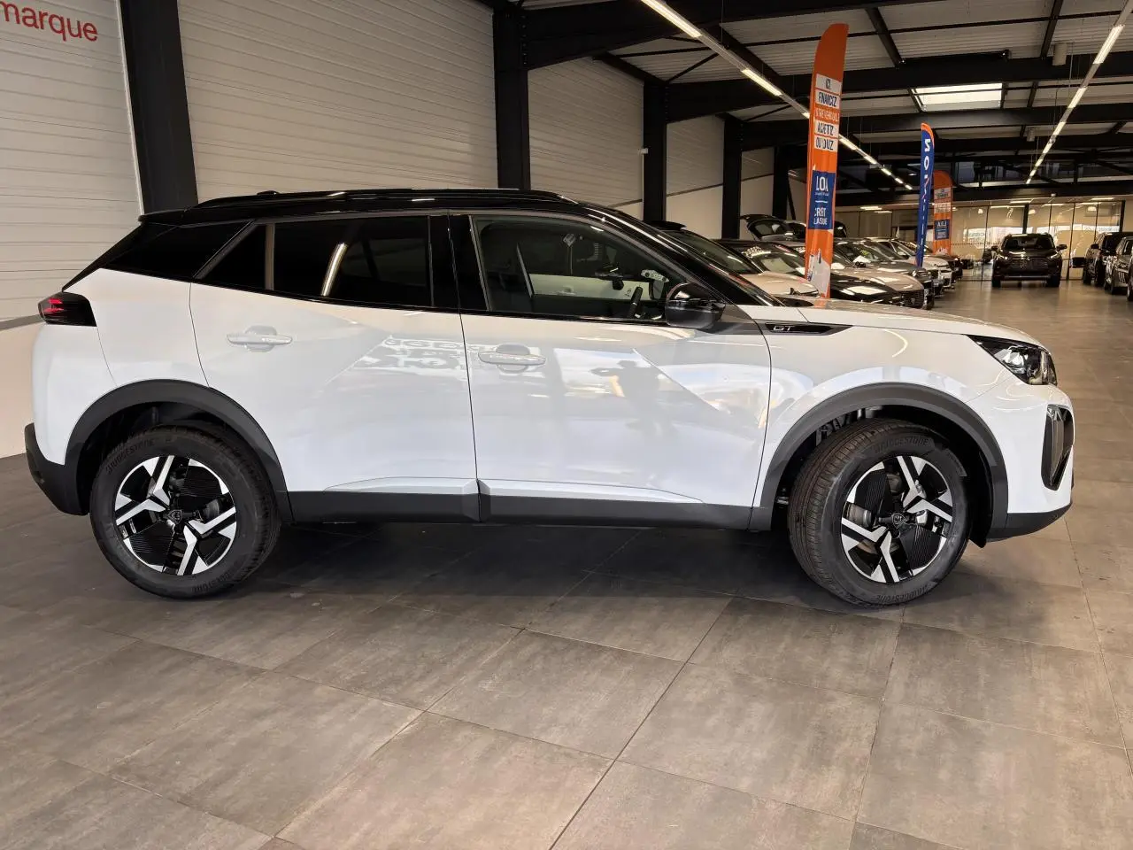 Profil droit du Peugeot 2008 blanc hybride 2025 en intérieur, avec toit noir et jantes distinctives bicolores.