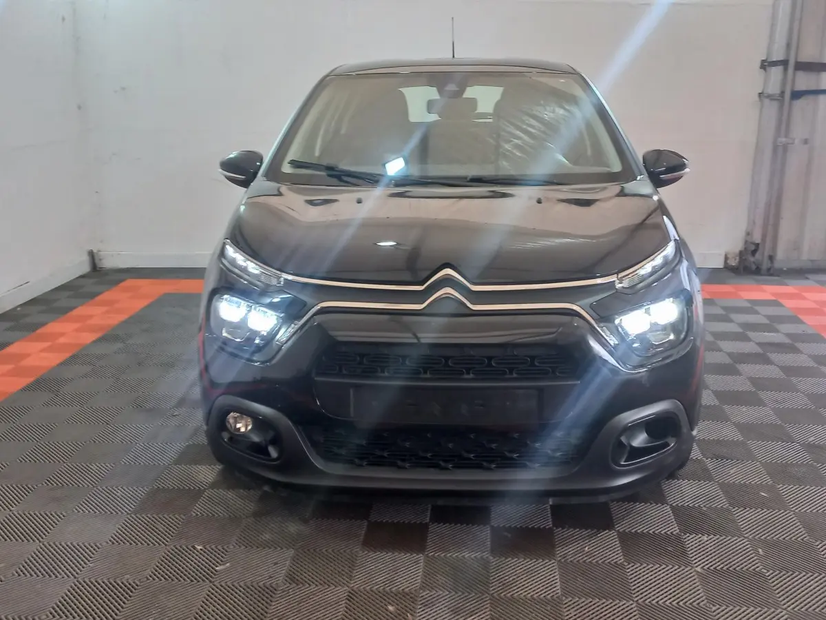 Vue avant d'une Citroën C3 noire 2024 avec phares LED allumés dans un garage au sol damier noir et orange.