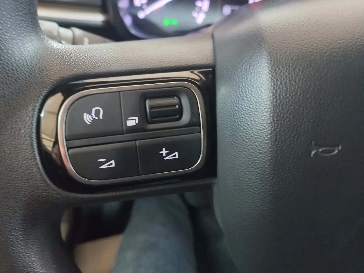 Gros plan sur les commandes vocales et volume du volant noir de la Citroën C3 BlueHDi 2024.