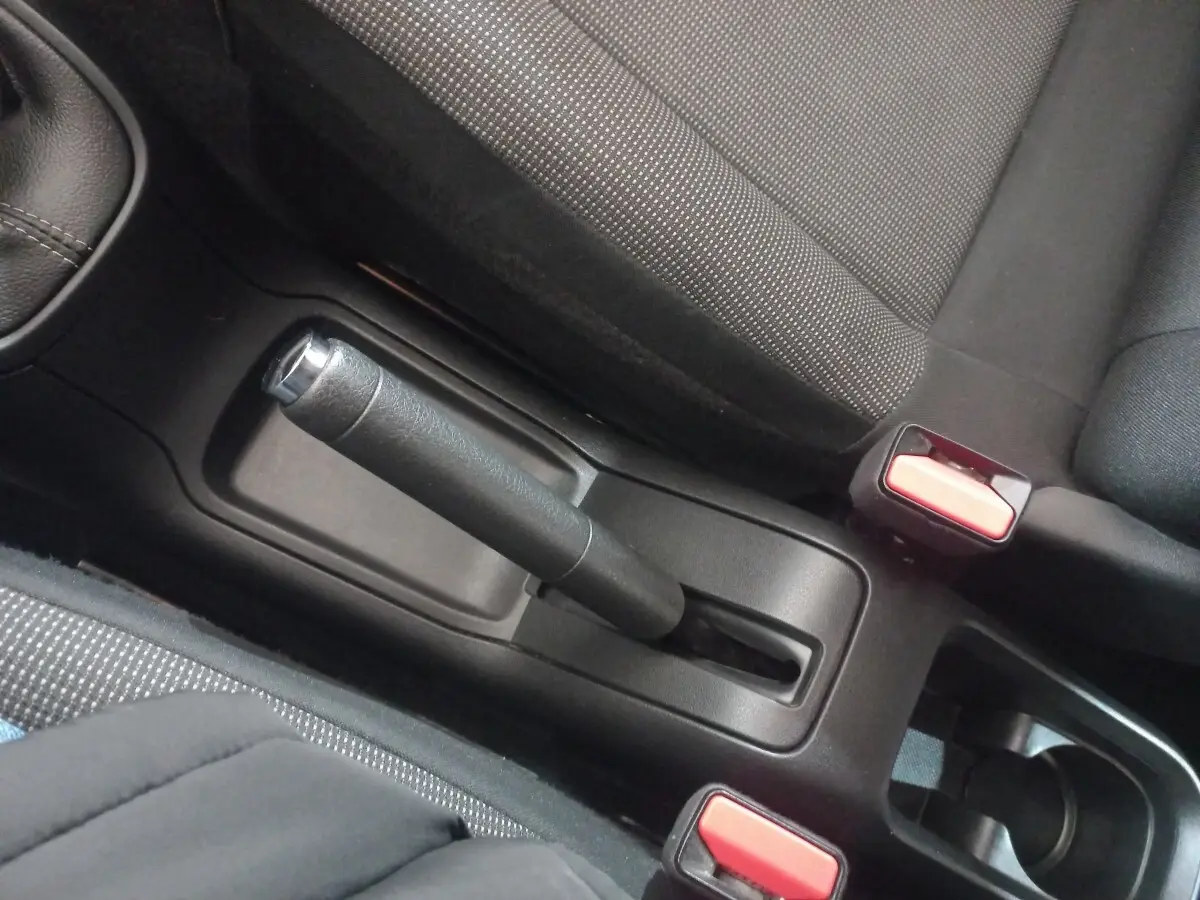 Vue rapprochée de la poignée de frein à main noir et des ceintures de sécurité rouges dans l’habitacle d’une Citroën C3 noire.