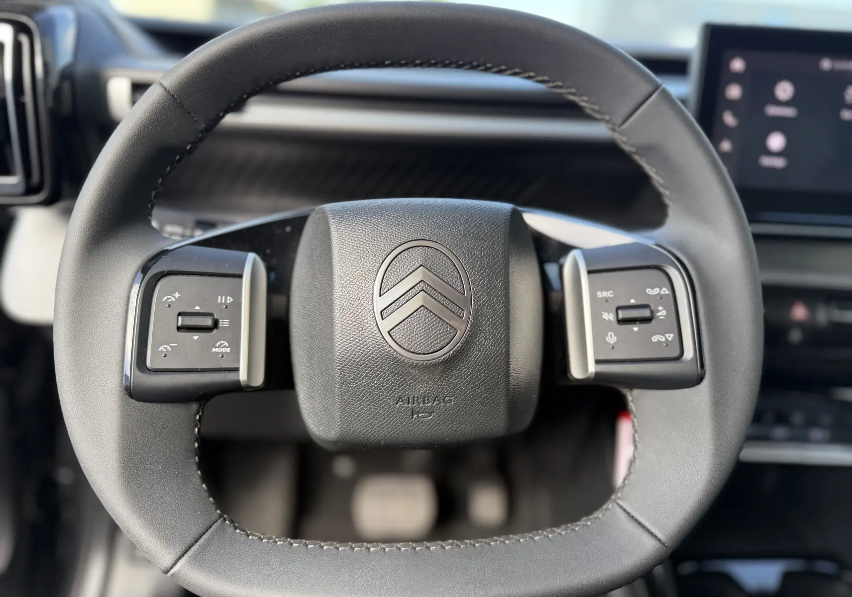 Gros plan sur le volant cuir noir du Citroën C3 Aircross électrique 2025 avec commandes intégrées et logo central.