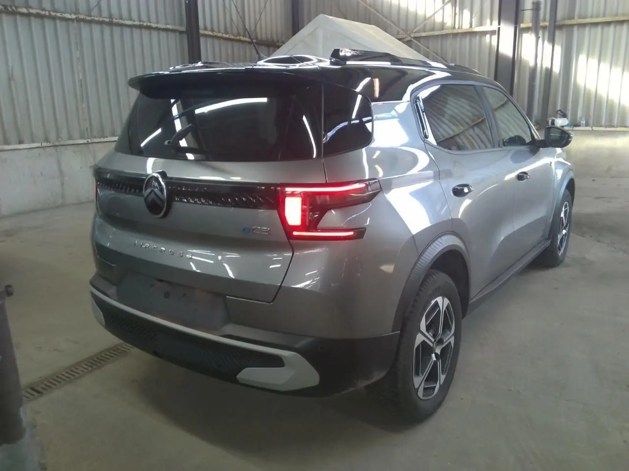 Vue 3/4 arrière droite d'une Citroën C3 Aircross électrique gris Mercury avec toit noir et feux arrière LED allumés.