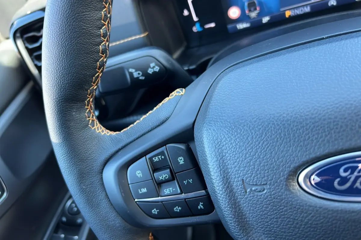 Gros plan sur le volant cuir noir avec surpiqûres marron du Ford Ranger Wildtrak Plus 2026, boutons multifonctions visibles.