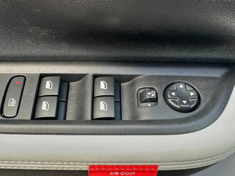 Gros plan sur les commandes de lève-vitres et réglage des rétroviseurs côté conducteur d'une Citroën C3 gris Mercury.