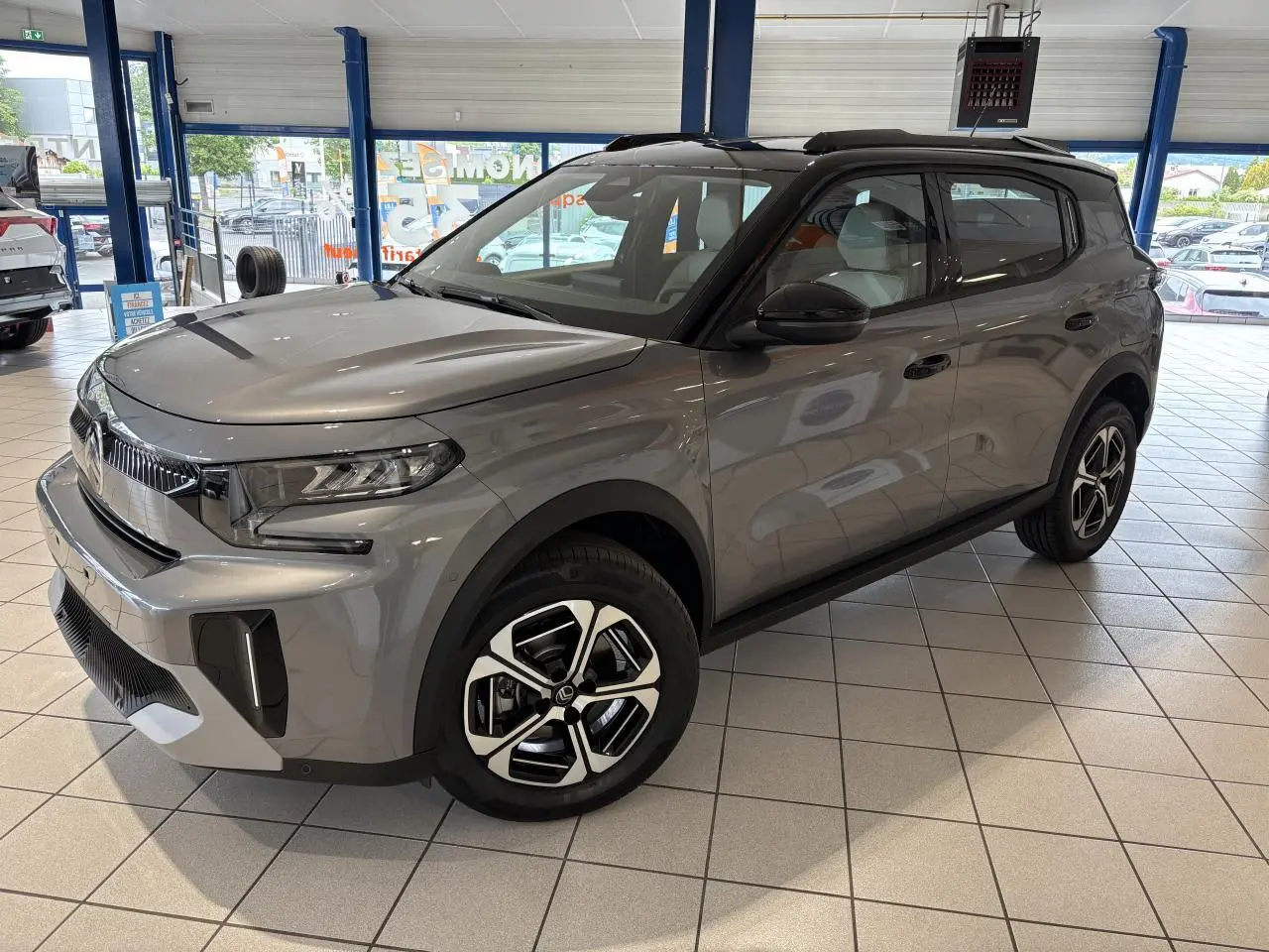 Citroën C3 Aircross 2026 gris métallisé avec toit noir, vue 3/4 avant droit en showroom intérieur.
