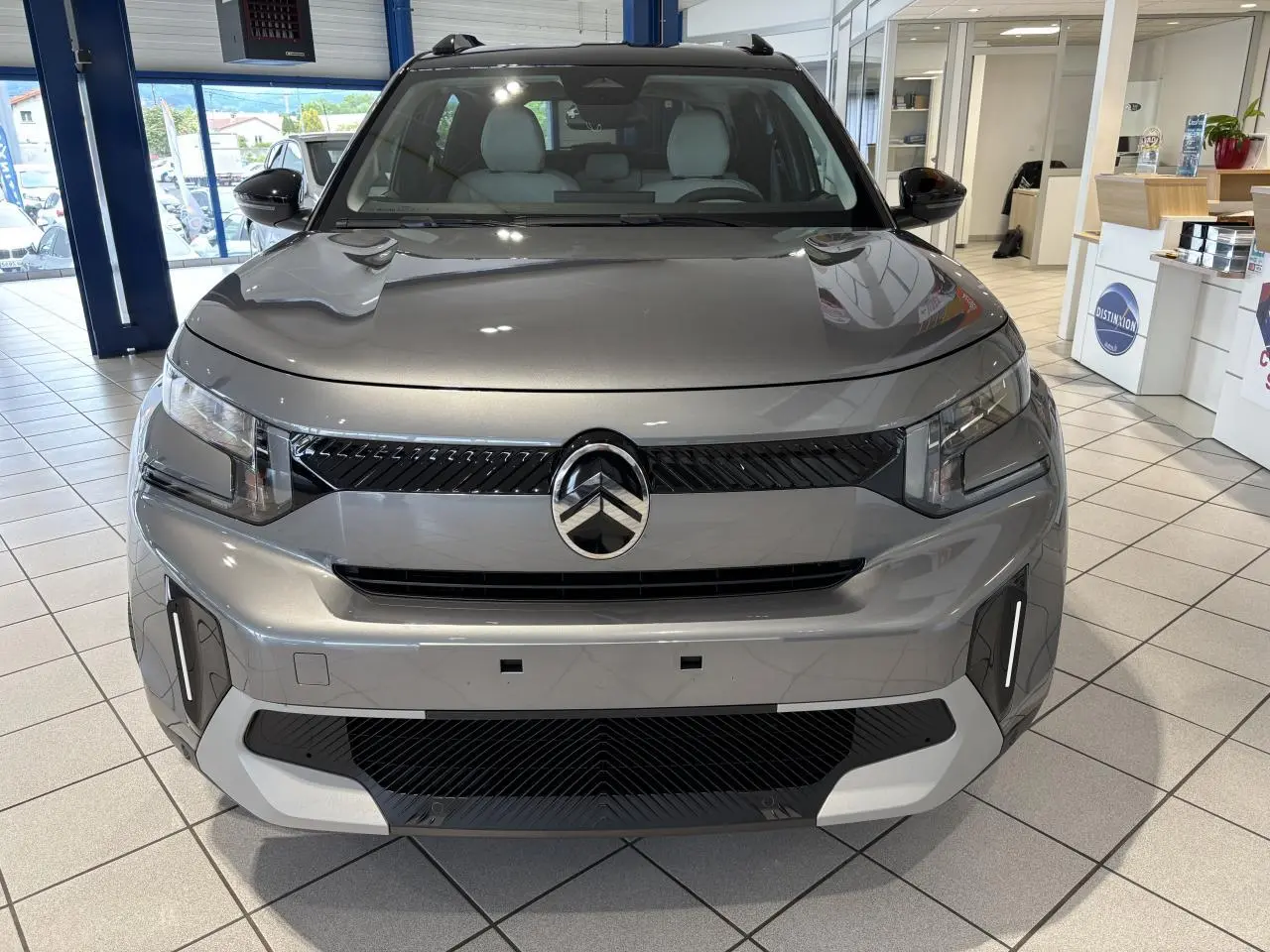 Vue avant d’un Citroën C3 Aircross 2026 gris métallisé avec toit noir, en showroom lumineux.