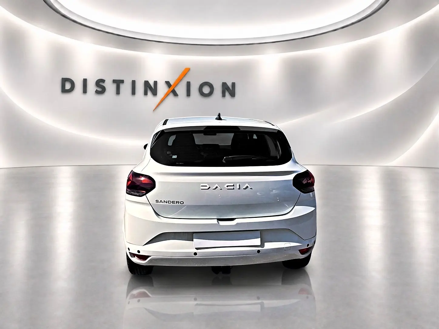 Vue arrière d'une Dacia Sandero blanche 2025 dans un showroom avec logo Distinxion en arrière-plan.
