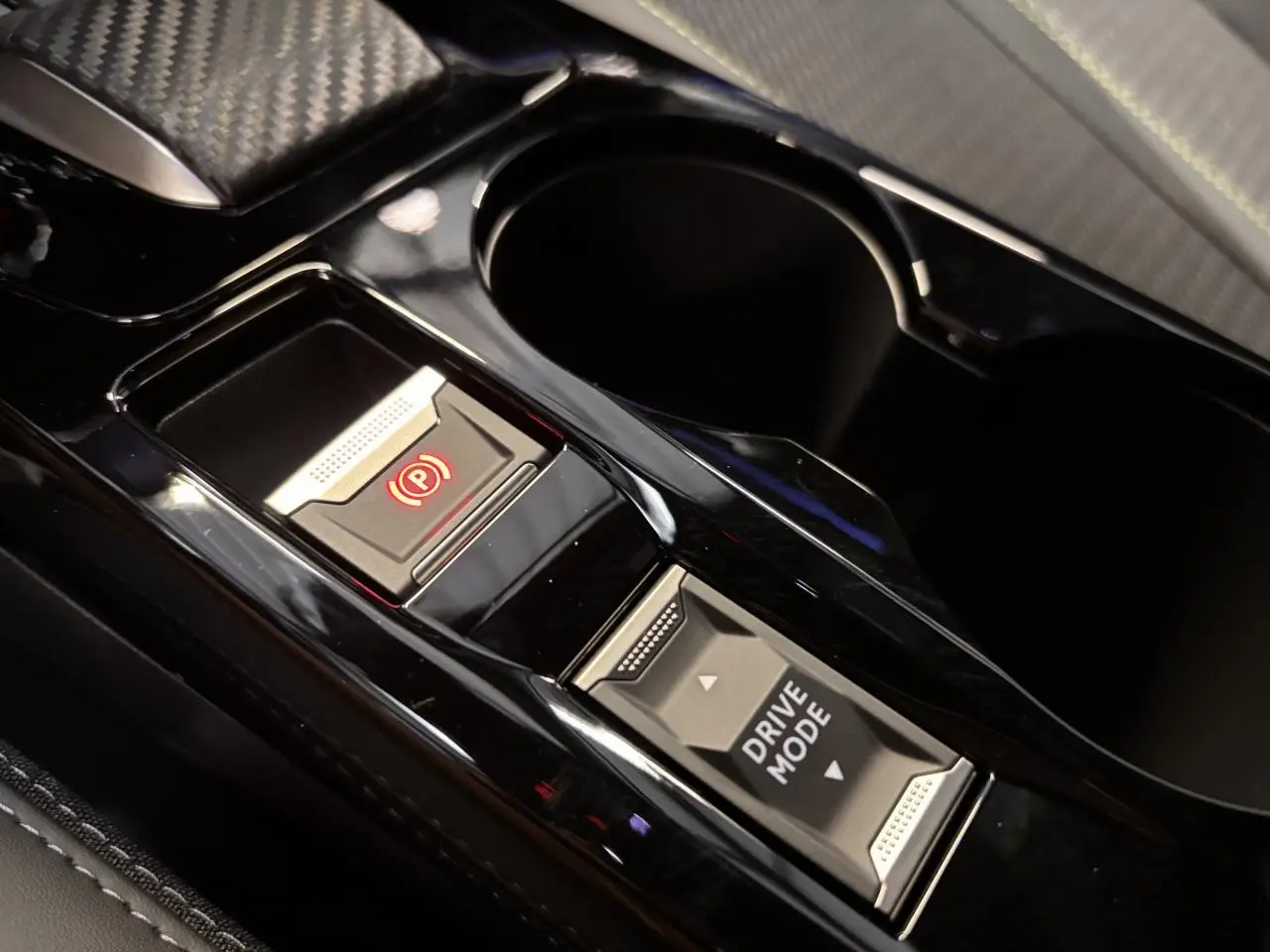 Gros plan sur la console centrale noire brillante du Peugeot 2008 gris, avec bouton frein à main électrique et sélection drive mode.