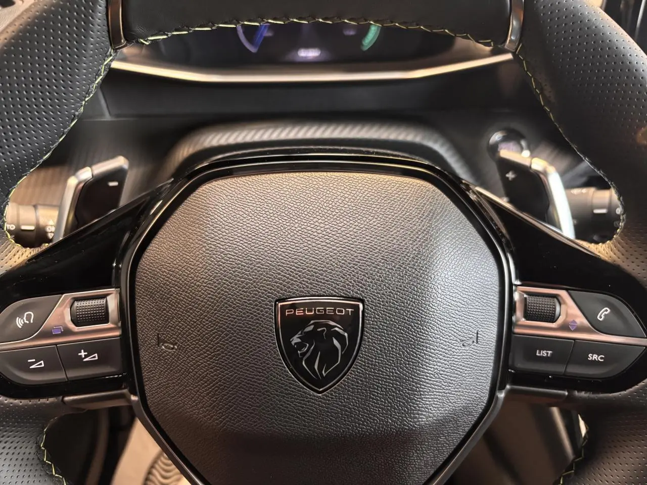 Gros plan sur le volant noir perforé du Peugeot 2008 gris, avec commandes intégrées et logo lion central.