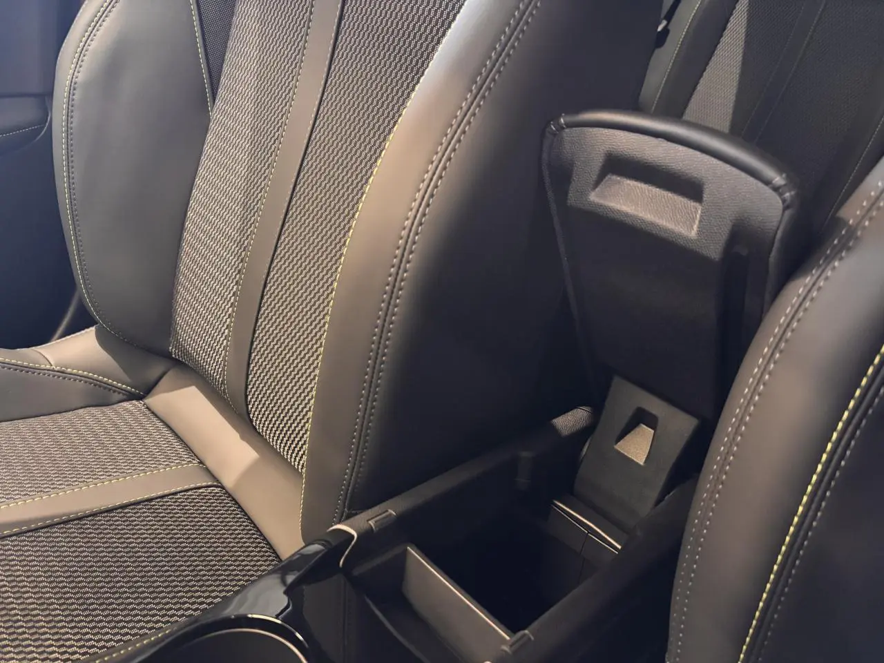 Détail de la console centrale ouverte entre les sièges avant en cuir et tissu gris du Peugeot 2008 hybride 2025.