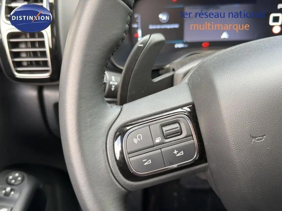Gros plan sur le volant cuir multifonctions du Citroën C5 Aircross platine, avec commandes audio et palettes au volant visibles.