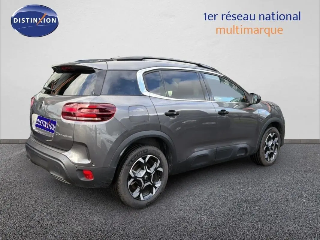 Vue 3/4 arrière droite d'un Citroën C5 Aircross platine avec barres de toit et jantes aluminium distinctives.