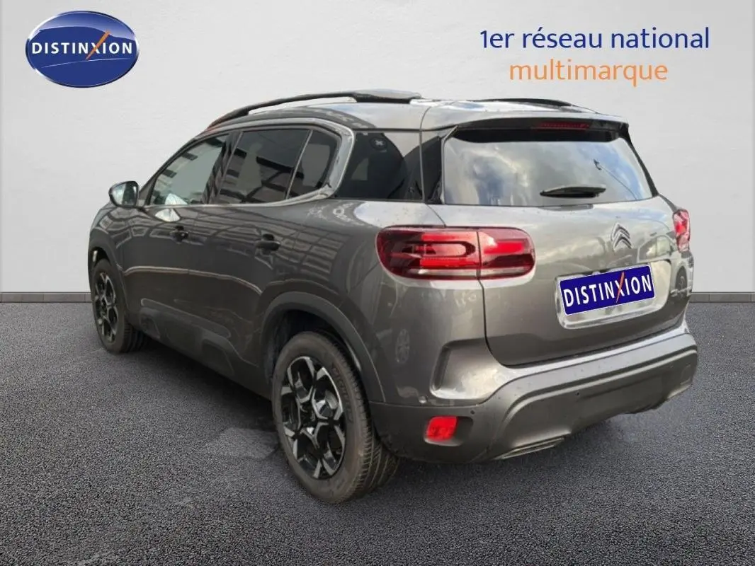 Vue 3/4 arrière droite d’un Citroën C5 Aircross platine 2025 avec barres de toit et jantes aluminium noires.