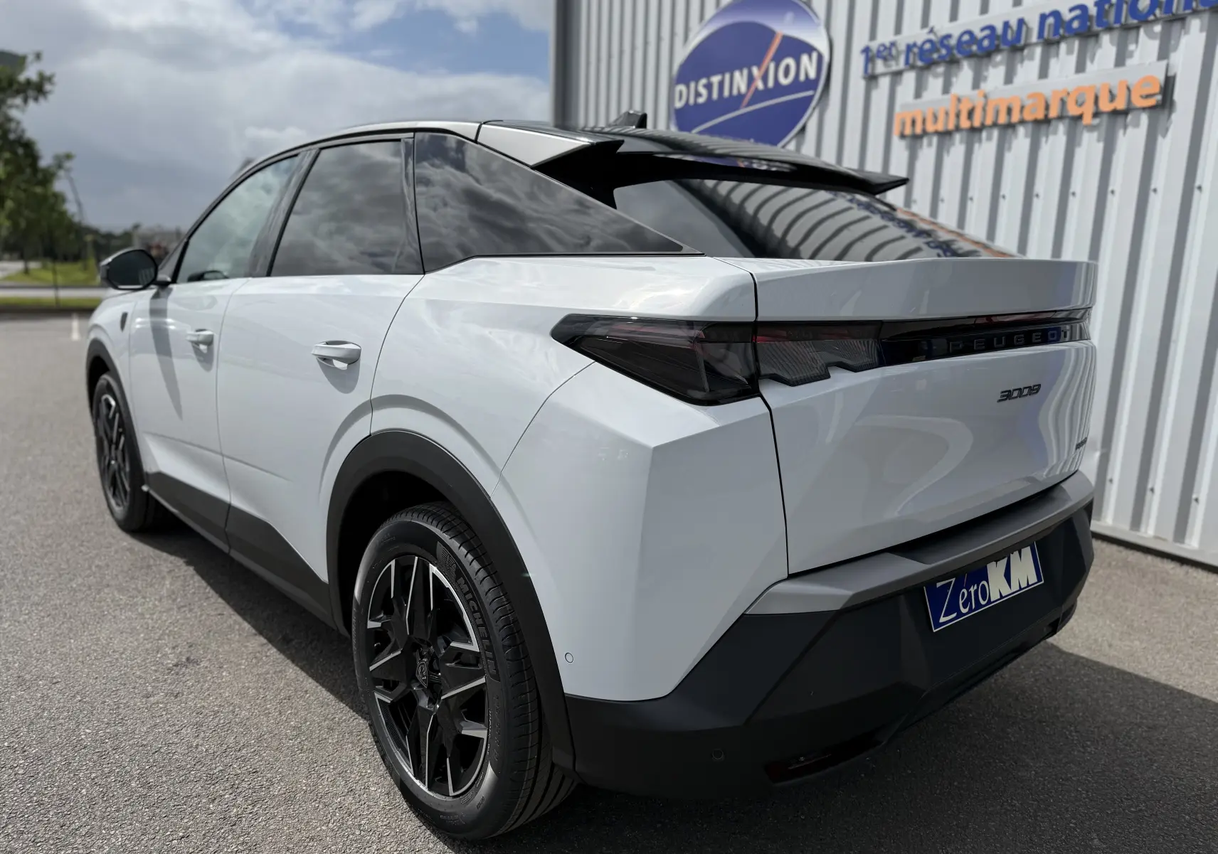 Vue 3/4 arrière droite du Peugeot 3008 Hybrid blanc Okenite avec toit noir et jantes noires distinctives.