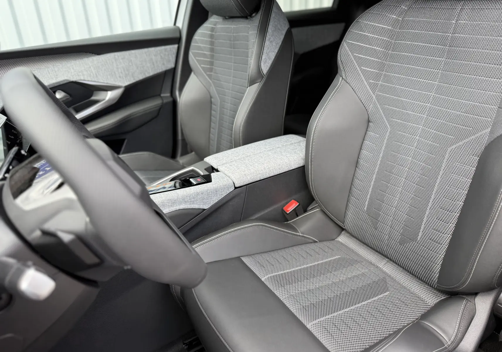 Vue intérieure rapprochée des sièges avant gris et noir du Peugeot 3008 Hybrid 2026 avec console centrale et volant partiel.