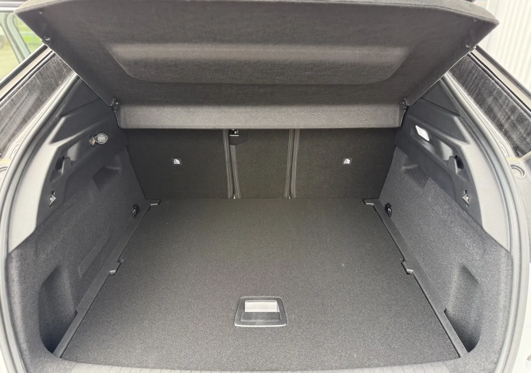 Coffre ouvert vu de l'arrière d'un Peugeot 3008 Hybrid blanc avec intérieur de coffre noir et cache-bagages relevé.