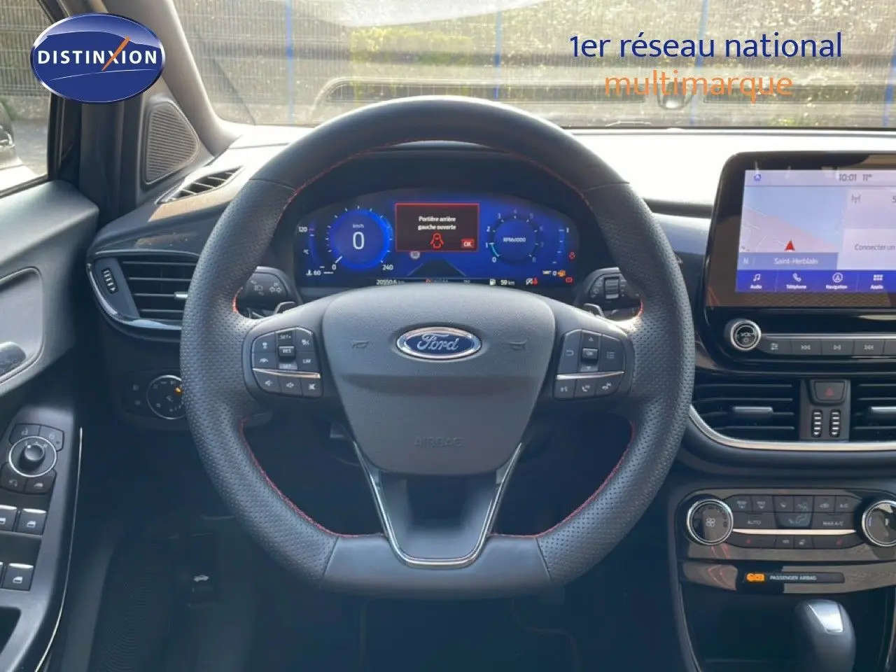 Vue intérieure centrée sur le volant noir avec surpiqûres rouges et tableau de bord numérique du Ford Puma 2023.