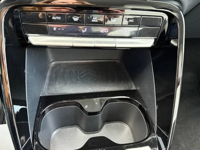 Gros plan sur la console centrale noire brillante de la Citroën C3 2025, avec commandes climatisation et support smartphone.