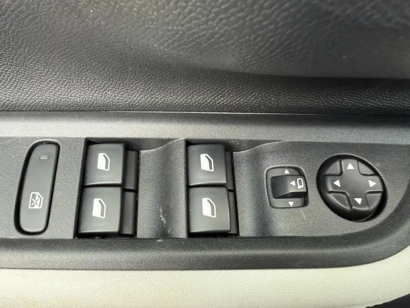 Gros plan sur les commandes de lève-vitres et réglage des rétroviseurs côté gauche intérieur d'une Citroën C3 Bright Blue 2025.