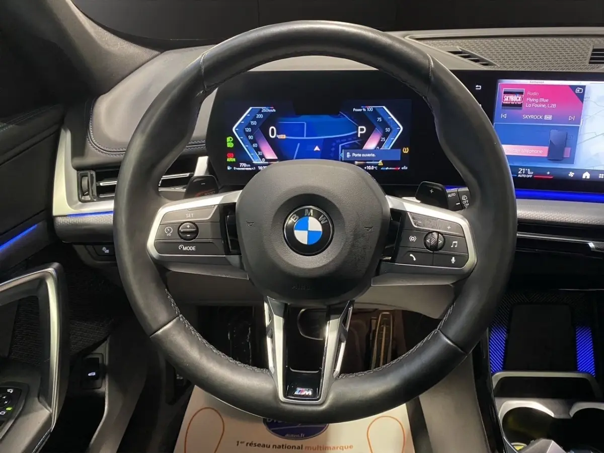 Vue intérieure centrée sur le volant cuir noir M Sport et l'écran digital du tableau de bord du BMW X1 2025.