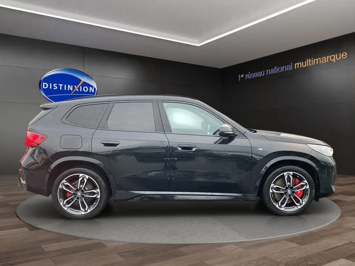 BMW X1 noir vue de profil côté gauche, avec jantes alliage et étriers de frein rouges visibles.