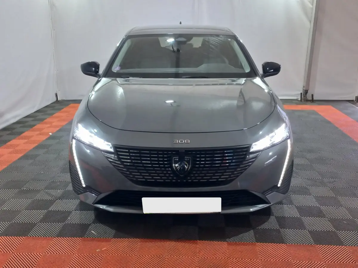Vue frontale d'une Peugeot 308 PHEV 180 E-EAT8 Allure gris foncé avec phares LED allumés dans un garage.