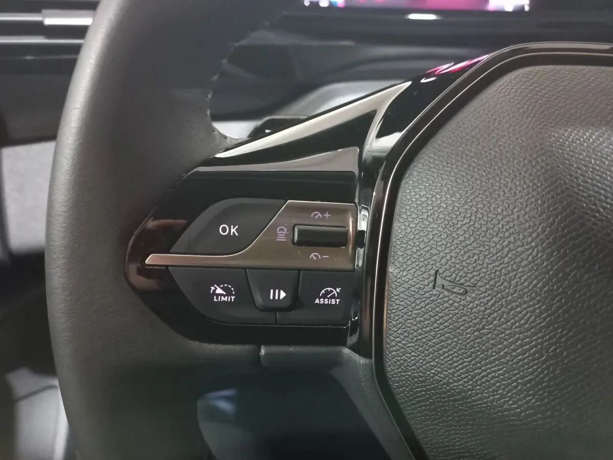 Gros plan sur le côté gauche du volant cuir de la Peugeot 308 PHEV 180 E-EAT8 Allure 2025 avec commandes intégrées.
