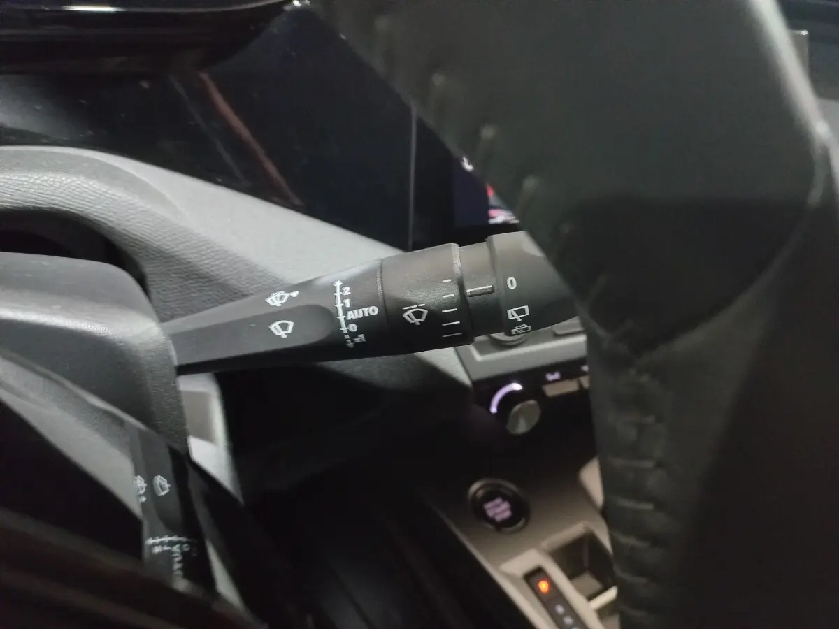 Gros plan sur la manette d’essuie-glace à gauche du volant cuir dans l’habitacle sombre d’une Peugeot 308 PHEV 2025.