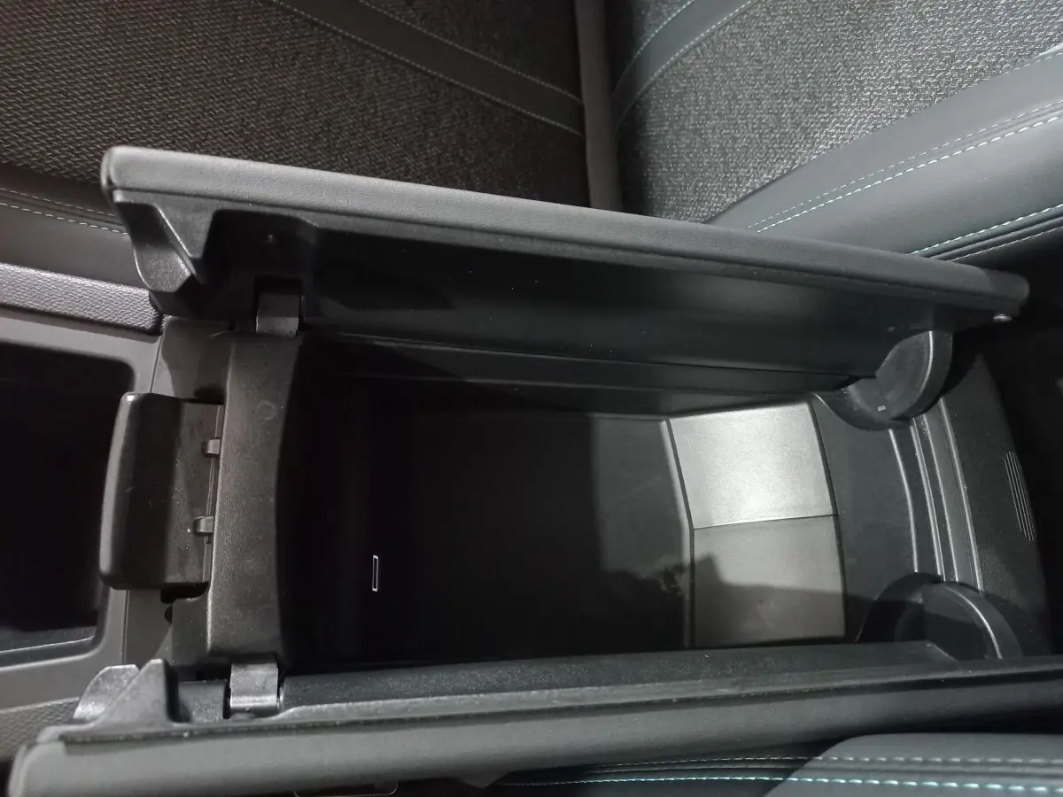 Vue rapprochée de la console centrale ouverte de la Peugeot 308 PHEV 180 Allure, intérieur gris foncé avec surpiqûres bleues.