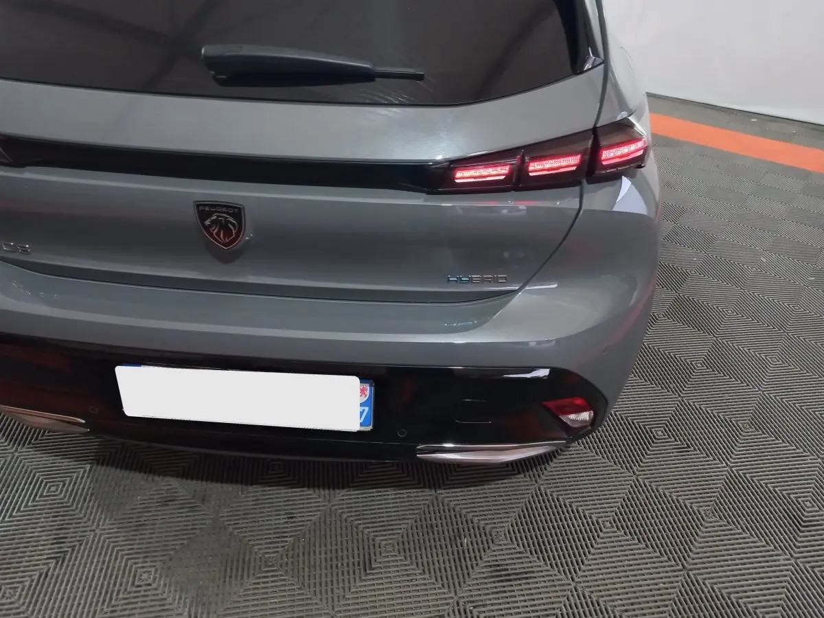 Vue arrière de la Peugeot 308 PHEV gris foncé avec feux LED allumés et logo hybride visible sur le coffre.