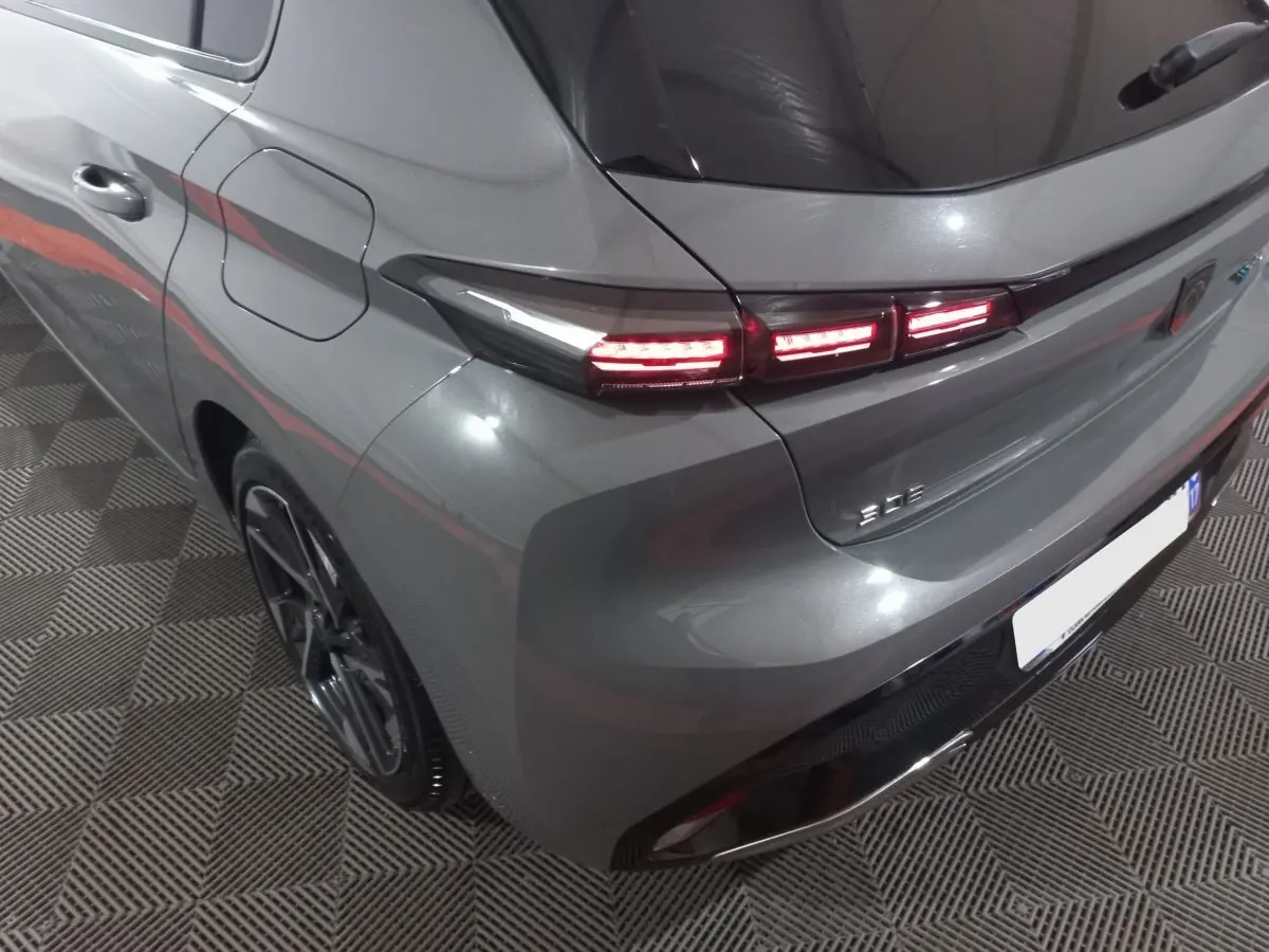 Vue 3/4 arrière droite d’une Peugeot 308 PHEV 180 E-EAT8 Allure gris foncé avec feux arrière LED allumés.