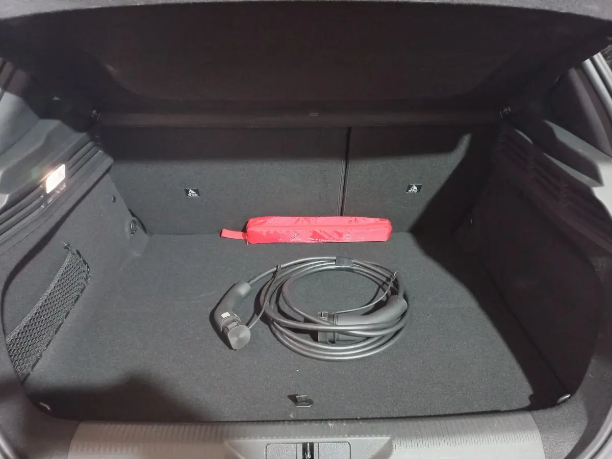 Coffre ouvert d’une Peugeot 308 PHEV gris foncé, montrant un câble de recharge noir et une trousse de secours rouge.