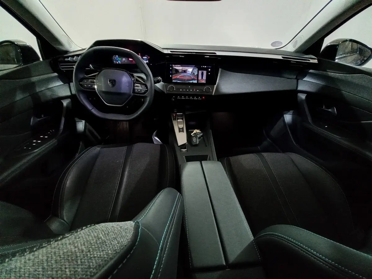 Intérieur noir de la Peugeot 308 PHEV 2025, vue avant centrée sur le volant, écran tactile et console centrale.