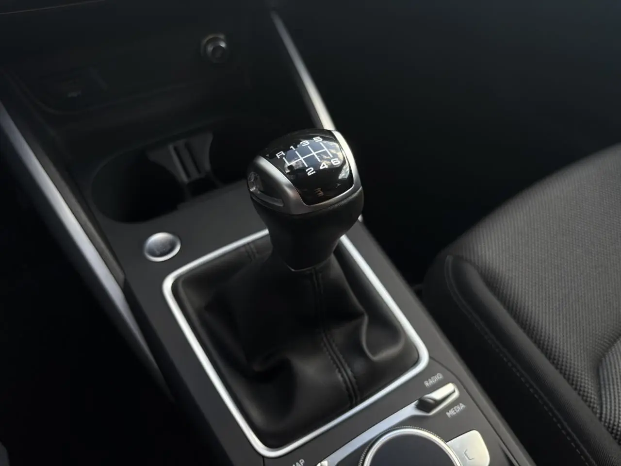 Gros plan sur le levier de vitesses manuel noir de l'Audi Q2 30 TFSI S-Line, avec console centrale et siège en tissu visible.