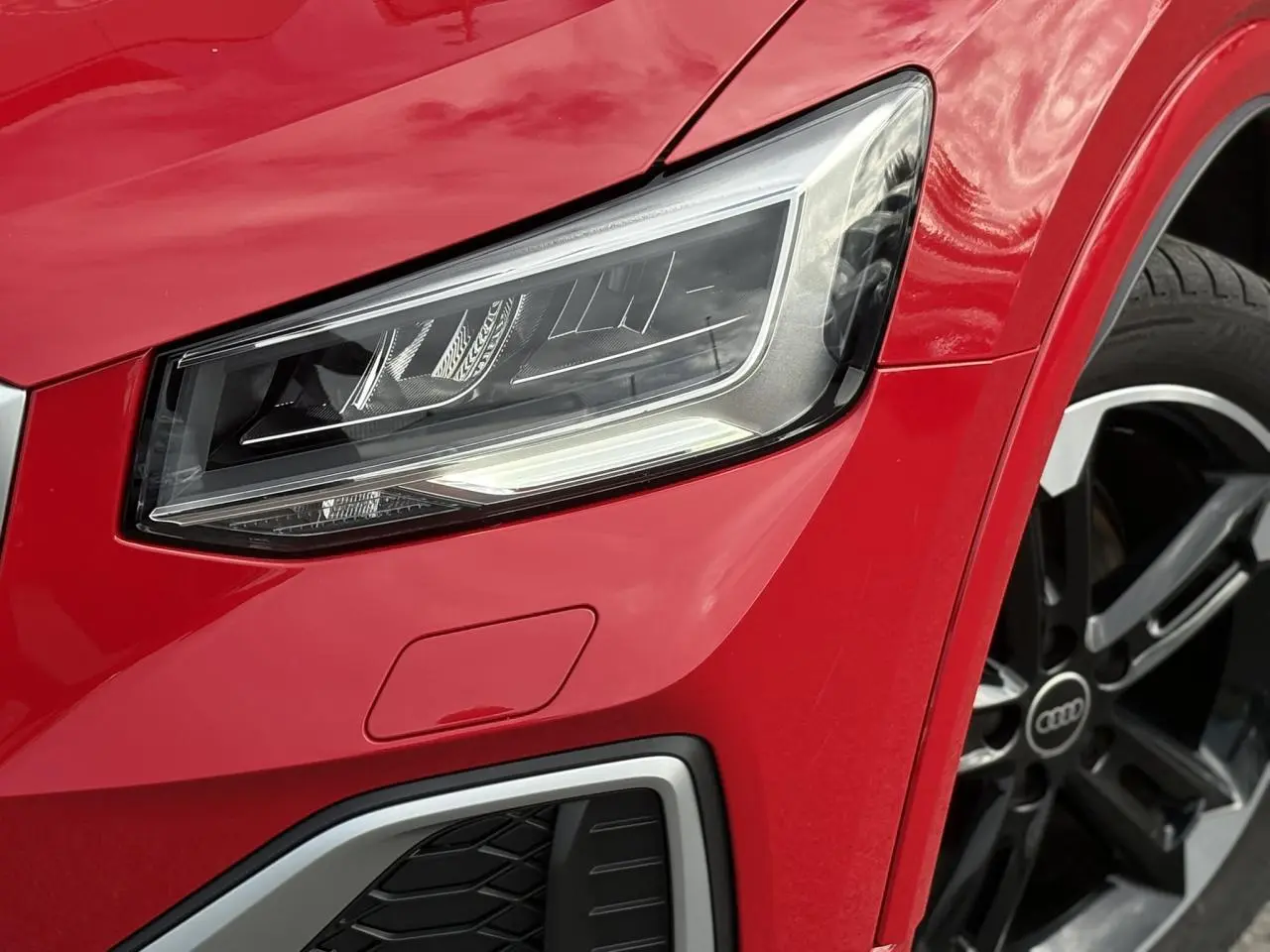 Gros plan sur le phare avant droit et la jante alliage noir poli du SUV Audi Q2 rouge Progressif.