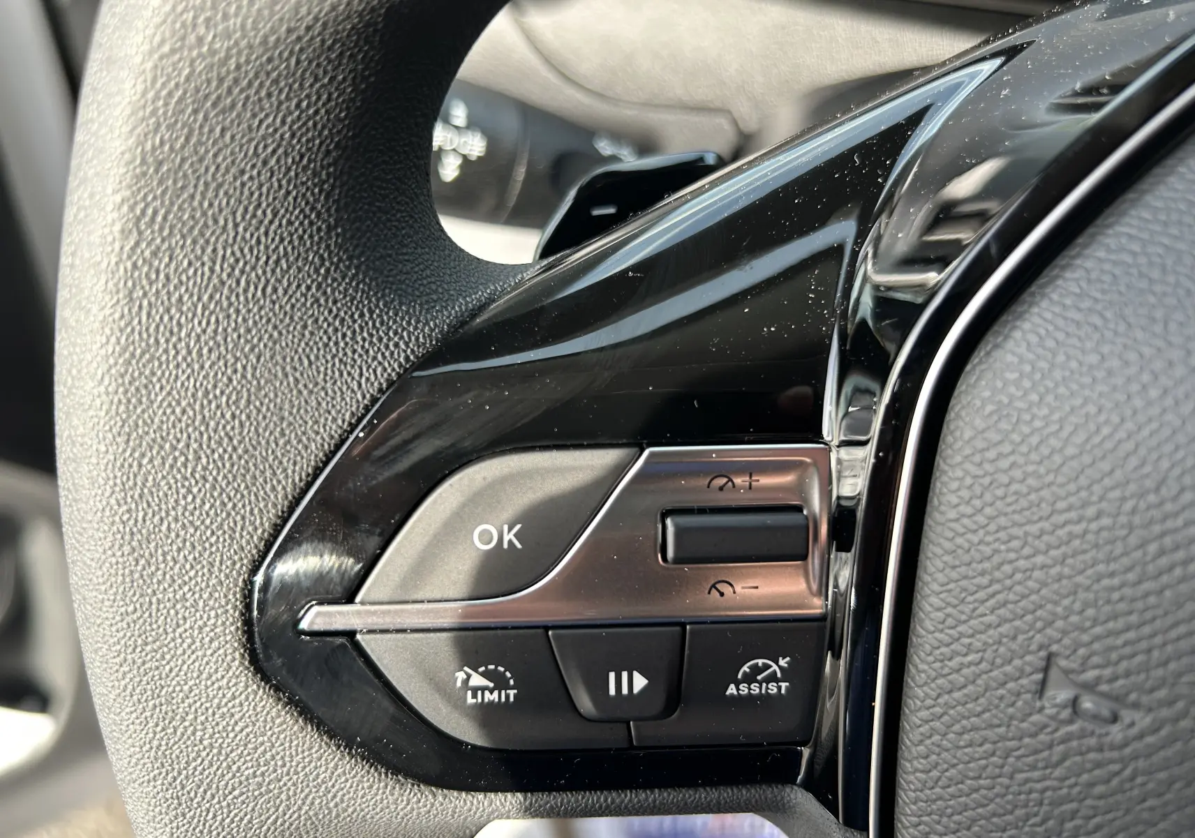 Gros plan sur les commandes noires du volant du Peugeot Partner Fourgon blanc 2025, avec boutons de limitation et assistance.