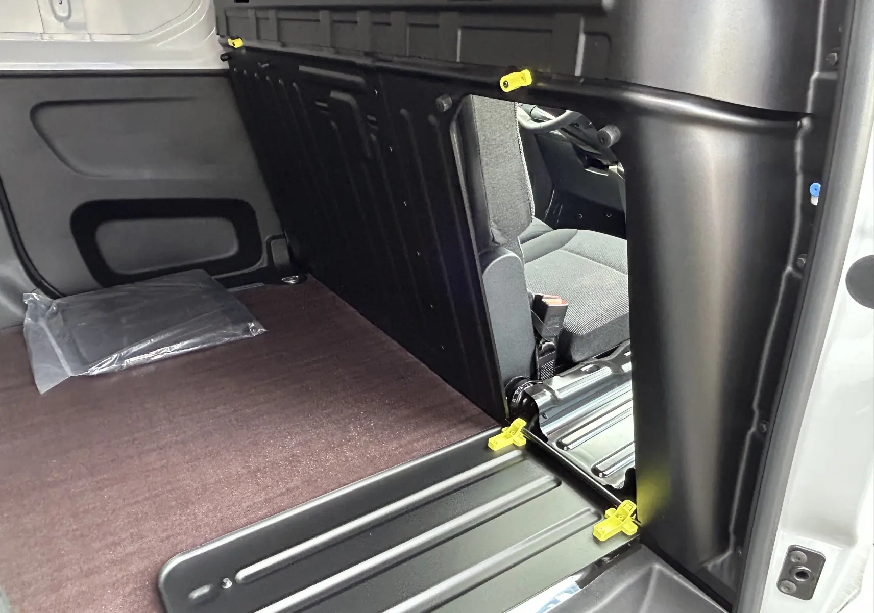 Vue intérieure du plancher bois brun et cloison noire du Peugeot Partner Fourgon blanc, avec siège conducteur gris visible.